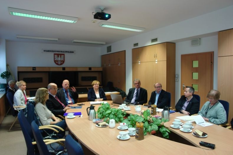 Grupa osób siedząca przy owalnym stole. W tle na ścianie godło województwa.