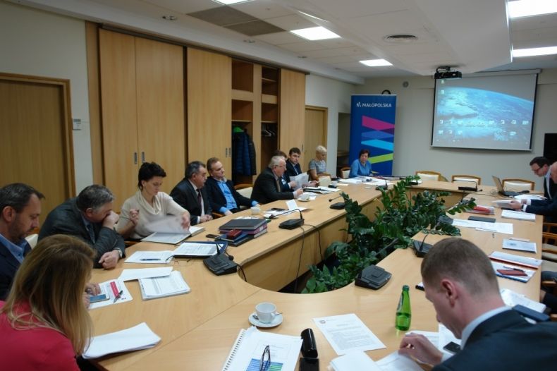 Grupa osób siedzących przy stole, w tle na ekranie wyświetlana jest prezentacja.