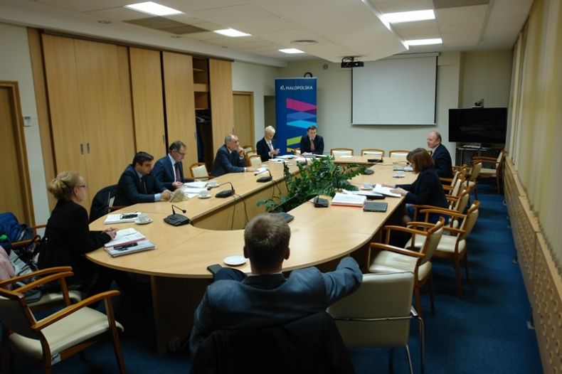 Grupa osób siedzących przy długim owalnym stole. Na końcu sali ekran, na którym wyświetlana jest prezentacja.