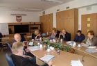 Grupa osób siedzących przy stole. Na ścianie w tle godło Małopolski.