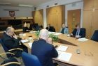 Grupa osób siedzących przy stole. W tle na ścianie wisi godło Małopolski.