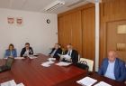 Grupa osób siedzących przy stole. Na ścianie godła Małopolski i Polski.