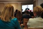 pomiędzy głowami dwóch uczestniczek sympozjum w tle widoczny jest duży monitor z prelegentem