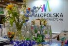 na pierwszym planie wazon z kwiatami i butelki z wodą mineralną z Małopolski, a w tle na białej ścianie logo Małopolska Innowacyjna