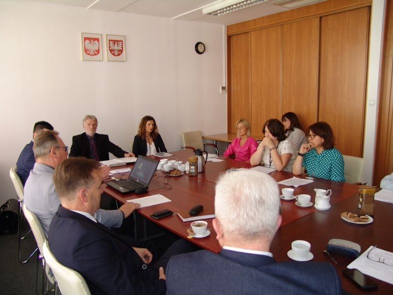 Grupa osób siedzących przy stole. Na ścianie godła Małopolski i Polski.