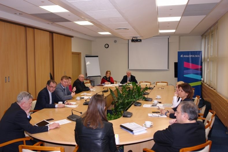 Grupa osób siedzących przy owalnym stole.