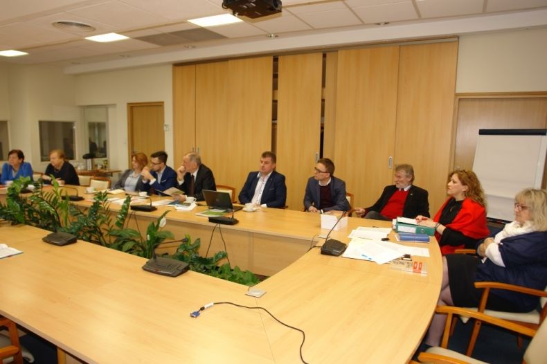 Grupa osób siedzących przy trzech prostokątnych stołach.