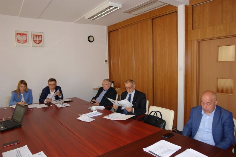 Grupa osób siedzących przy stole. Na ścianie godła Małopolski i Polski.
