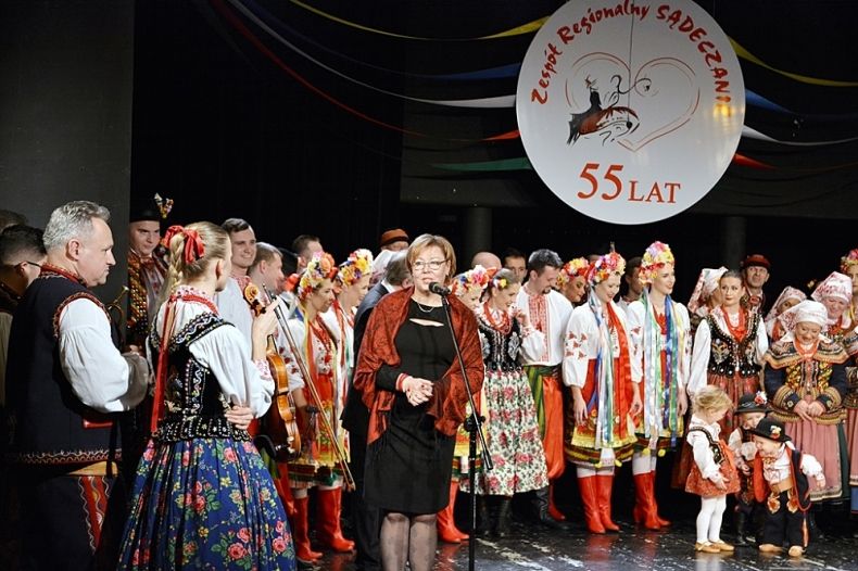 Grupa ludzi stojących na scenie. W tle na ścianie logo zepołu Sądeczanie.