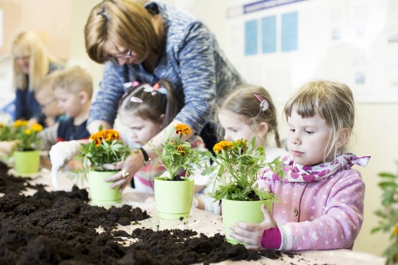 Na zdjęciu dzieci sadzące kwiatki w doniczkach