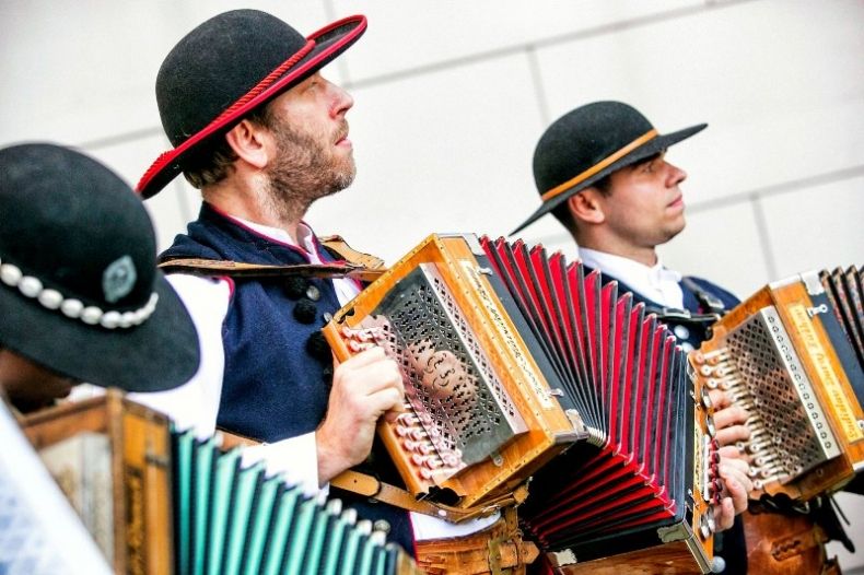 Zdjęcie przedstawia 3 mężczyzn w czapkach góralskich, grających na instrumencie Heligonka.