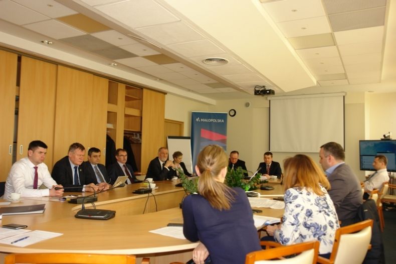 Grupa osób siedzących przy prostokątnym stole.