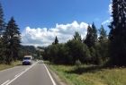 droga asfaltowa dla samochodów, na poboczu rosną drzewa, nad jezdnią jest błękitne niebo, w tle nadjeżdżający bus