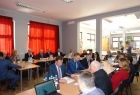 Grupa osób siedzących przy dwóch równoległych stołach.