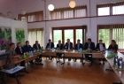 grupa osób siedzących na tle okna przy trzech stołach ułożonych w literę c.