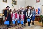 Dzieci i dorośli stoją obok siebie w pokoju. Dzieci trzymają papierowe torby w rękach 