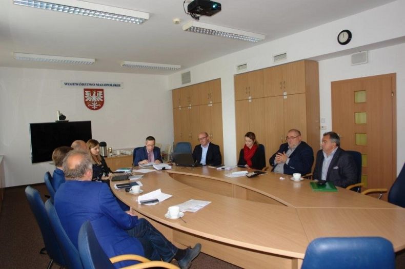 Grupa osób siedzących przy owalnym stole.