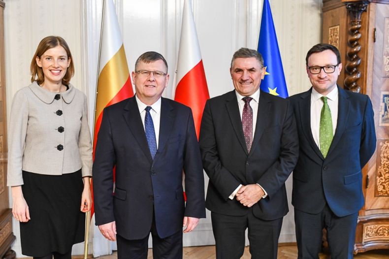 cztery osoby stoją na zdjęciu, z lewej strony kobieta i trzech mężczyzn. W tle flagi Małopolski, Polski i Unii Europejskiej