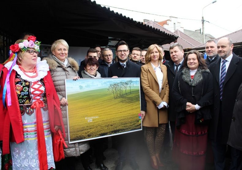 Grupa osób trzymających obraz przedstawiający pejzaż.