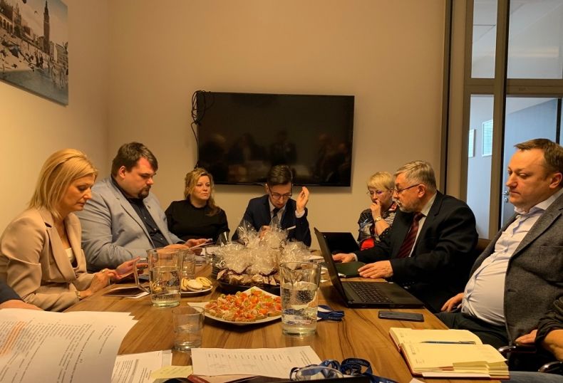 Grupa osób siedzących przy prostokątnym stole.
