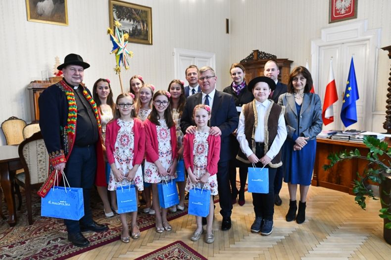 Dzieci i dorośli stoją obok siebie w pokoju. Dzieci trzymają papierowe torby w rękach 