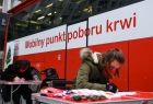 Pracownicy Urzędu Marszałkowskiego Województwa Małopolskiego siedzą przy dwóch stolikach i wypełniają ankietę przed oddaniem krwi. W tle krwiobus