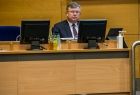 Marszałek Witold Kozłowski w trakcie obrad sejmiku województwa. Marszałek zasiada za zabudowanym stołem prezydialnym, na którym stoją dwa monitory.