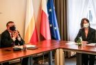 Marszałek Witold Kozłowski podczas spotkania dotyczącego Igrzysk Europejskich. Marszałek jest w maseczce ochronnej, zasiada za stołem konferencyjnym, obok znajdują się flagi Małopolski, Polski i Unii Europejskiej. Po prawej stronie, na tle okna, przy stol