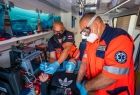 dwóch ratowników medycznych w pomarańczowych strojach w maseczkach, pracuje w karetce pogotowia ratunkowe, pomagając choremu