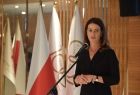 Konferencja prasowa na temat Igrzysk Europejskich 2023. Przemawia minister sportu Danuta Dmowska-Andrzejuk. Sylwetka na tle flag narodowych