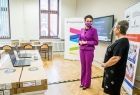 Dwie eleganckie kobiety: Marta Malec-Lech z zarządu województwa oraz dyrektor szkoły stoją przed ławką szkolną w klasie, na której leżą nowe laptopy.