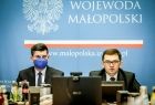 Wicemarszałek Łukasz Smółka i wojewoda Łukasz Kmita za stołem konferencyjnym. Za nimi błękitna ściana z orłem w koronie i napisem wojewoda małopolski