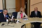 Trzy osoby siedzace za stołem. W środku kobieta zmikrofonem. Z lewej strony mężczyzna w garniturze i w okularach, przed nim mikrofony. Z prawej strony mężczyzna w garniturze