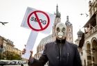 mężczyzna w masce gazowej na twarzy i kurtce skórzanej stoi z tabliczką z napisem smog. W tle Sukiennice i kościół Mariacki na Rynku Głównym w Krakowie