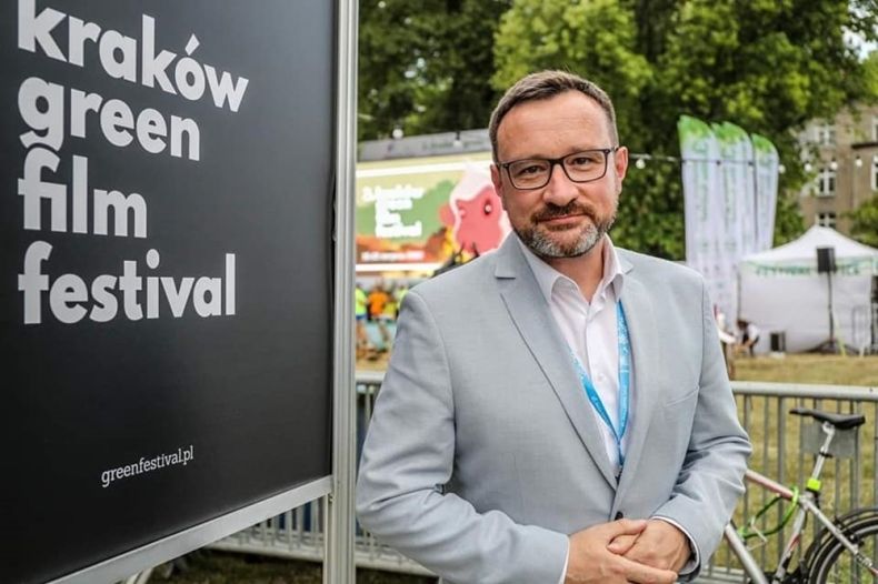 mężczyzna w garniturze stoi obok tablicy z napisem: Kraków green film festiwal