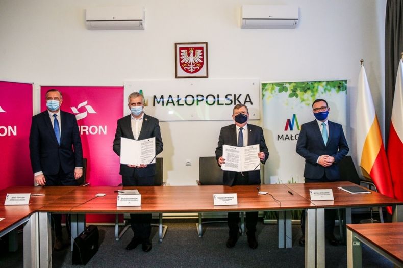 Czterech eleganckich mężczyzn w garniturach stoi za stołem, dwaj z nich trzymają podpisane umowy. W tle widoczne napisy: Małopolska, EkoMałopolska i Tauron.