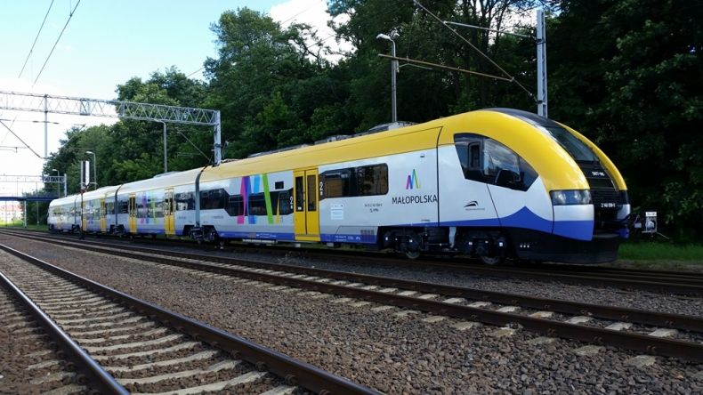 pociąg jadący po torach pomalowany na żółto, biało i niebiesko