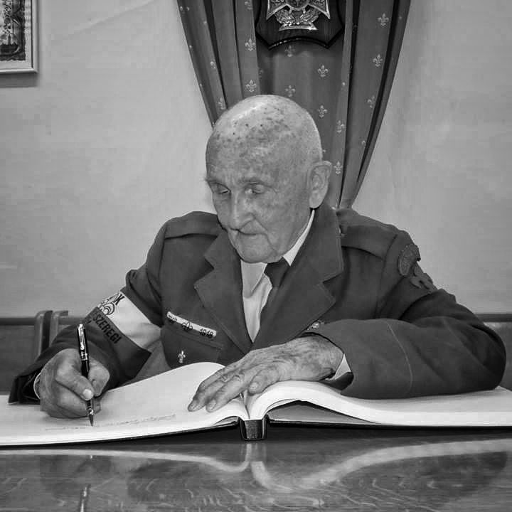 stary mężczyzna w mundurze wojskowym z odznaczeniami, podpisuje księgę