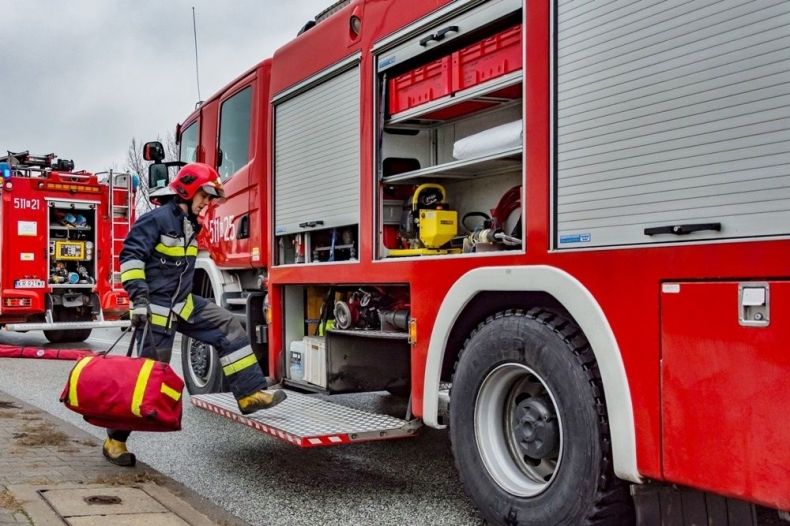 Zdjęcie ilustracyjne przedstawiające strażaka stojącego obok wozu strażackiego