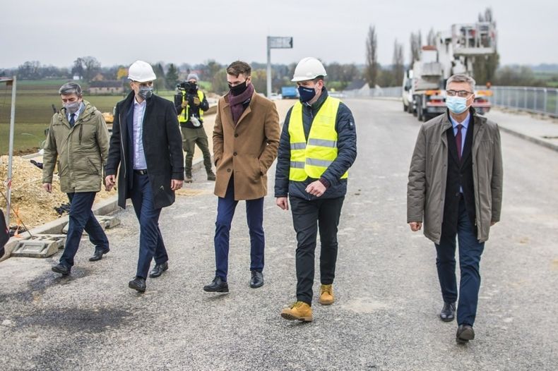 Pięciu mężczyzn, dwóch w białych kaskach, idą nowym mostem.