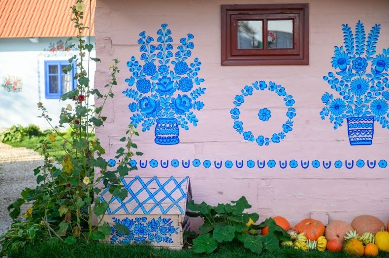 biała ściana drewnianej chaty z niebieskimi motywami ozdobniczymi 