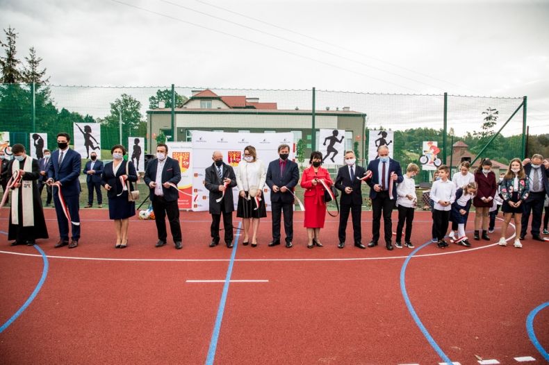 Grupa osób przecinających wstęgę na uroczystości otwarcia boiska sportowego