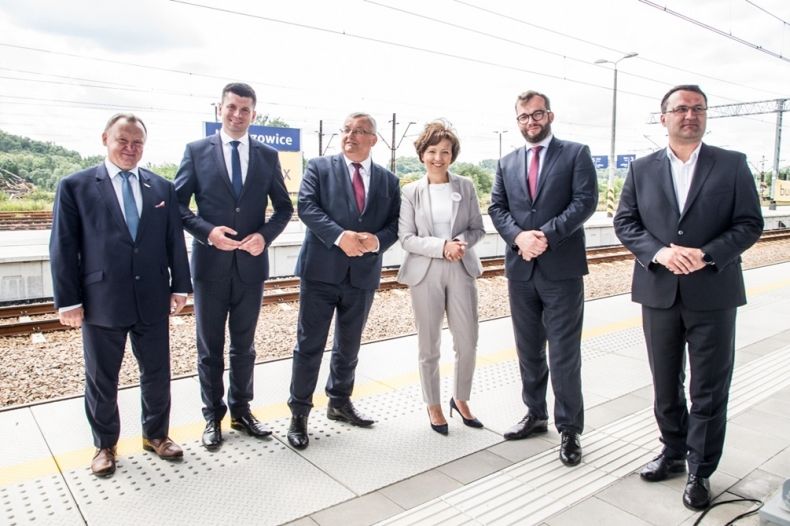 Pięciu mężczyzn w garniturach oraz kobieta w jasnym żakiecie na tle zmodernizowanego peronu kolejowego