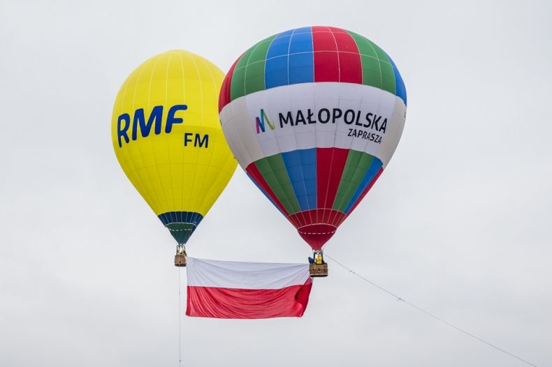 Dwa balony unoszące się w powietrzu, między nimi biało-czerwona flaga
