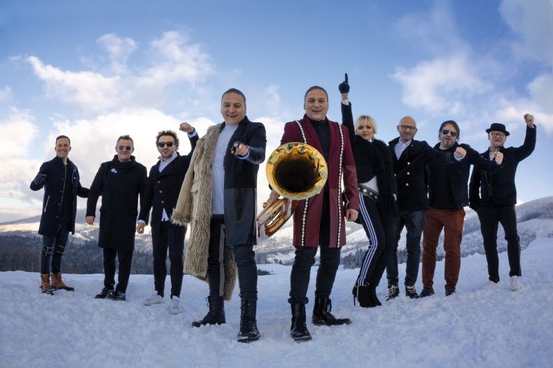Grupa osób pozuje na zaśnieżonej łące trzymając instrumenty muzyczne 