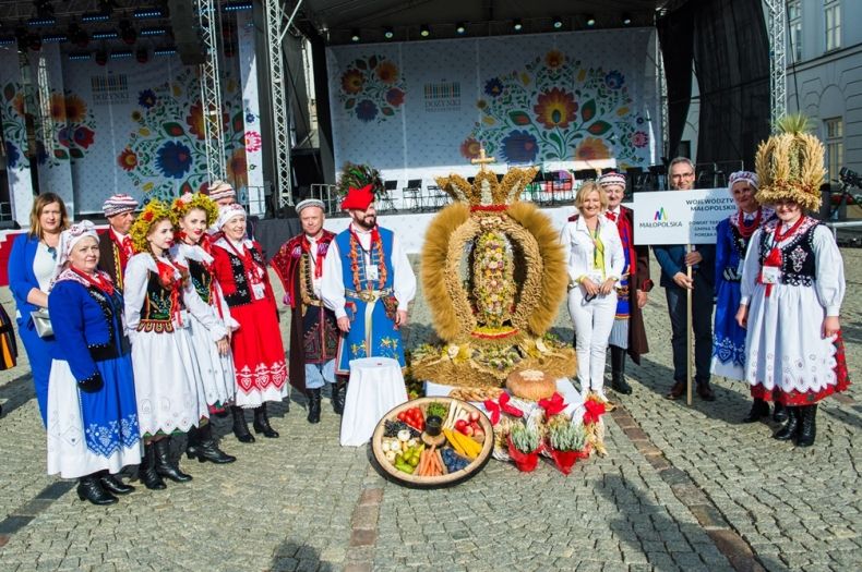 grupa ludzi w strojach ludowych z wieńcem ze zboża