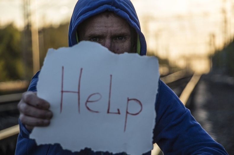 chłopak w bluzie z kapturem stoi na torach kolejowych z kartka z napisem help