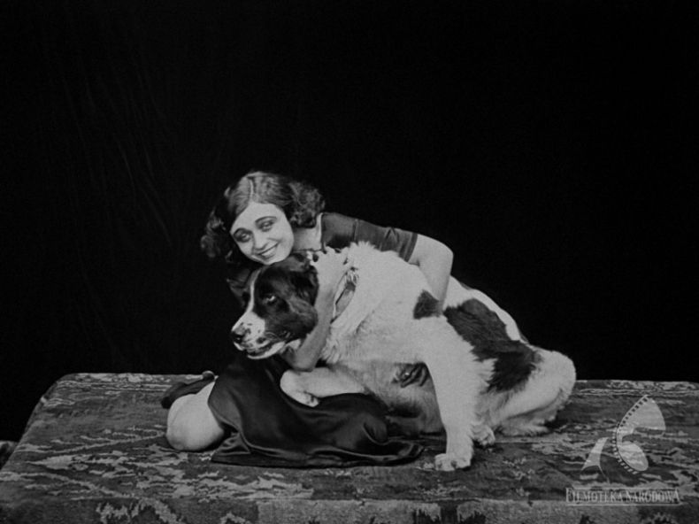 Czarno-białe zdjęcia. Kobieta siedzi na podłodze, uśmiecha się i przytula dużego psa.
