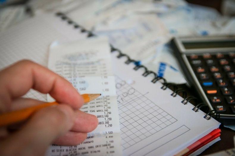 Zdjęcie przedstawia człowieka, rachunki i kalkulator