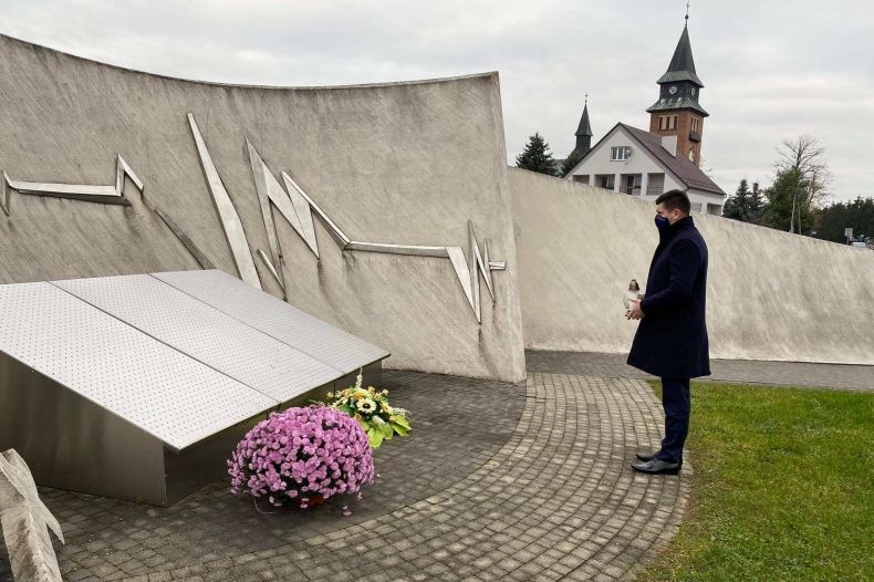 wicemarszałek Łukasz Smółka stoi przed pomnikiem upamiętniającym ofiary wypadków drogowych 